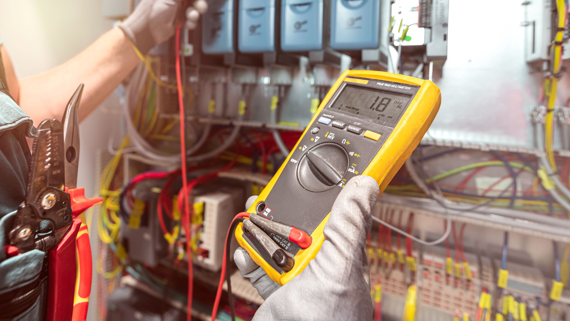 The electricians hand holding multimeter during checks the electrical wiring in the fuse box. Work in electrical industry.